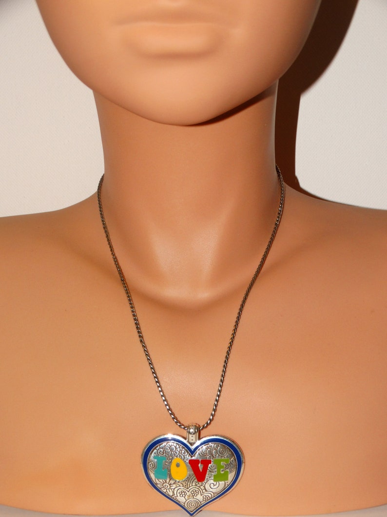 May include: A silver chain necklace with a heart-shaped pendant. The pendant is blue with a silver border and features the word "LOVE" in colorful enamel letters.