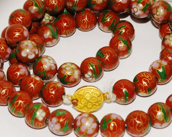 May include: A red and green enamel necklace with a gold clasp. The beads are round and have a floral design.