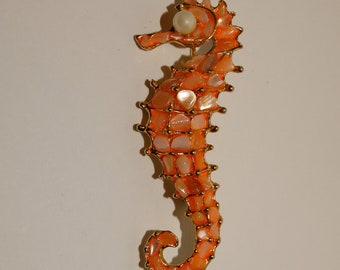 May include: A gold-toned seahorse brooch with a pearl accent. The seahorse is made of orange and white mosaic tiles.