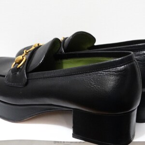 May include: Black leather platform loafers with a gold chain detail. The loafers have a green lining and a chunky heel.