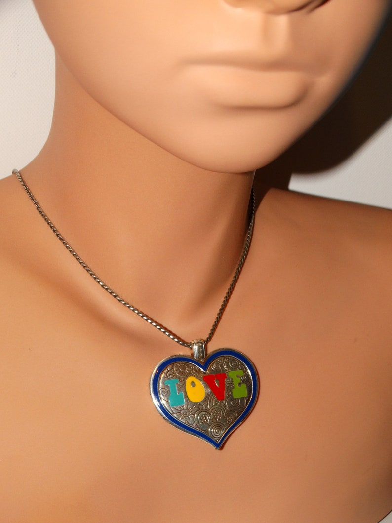 May include: A silver chain necklace with a heart-shaped pendant. The pendant is blue with a silver filigree design and the word "LOVE" spelled out in colorful enamel.