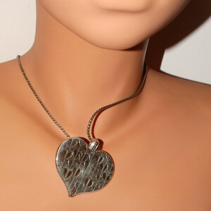 May include: A silver necklace with a heart-shaped pendant. The pendant has a detailed design of smaller hearts.