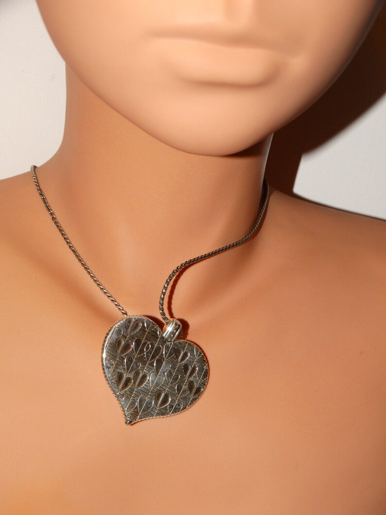 May include: A silver necklace with a heart-shaped pendant. The pendant has a detailed design of smaller hearts.
