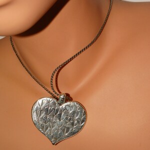 May include: A silver heart-shaped pendant necklace with a detailed design of smaller hearts. The necklace is on a black chain.