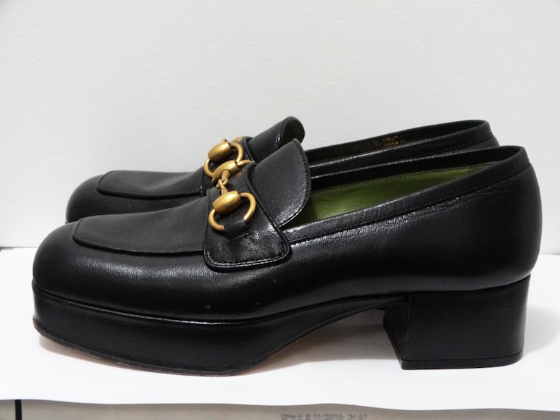 May include: Black leather platform loafers with gold chain detail. The loafers have a chunky heel and a square toe.