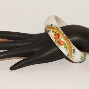 Könnte beinhalten: Weißes Porzellan-Armband mit goldenem und floralem Design. Die Blumen sind in Rot-, Orange-, Blau- und Grüntönen bemalt.