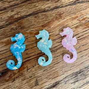 Puede incluir: Tres figuritas de caballitos de mar, una azul, una azul claro y una rosa. Cada caballito de mar tiene un acabado brillante.
