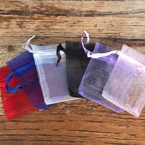 May include: Six small, sheer fabric bags in various colors, including red, blue, white, black, purple, and pink. The bags are made of a delicate, mesh-like material and have drawstring closures.