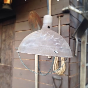 May include: "Indy" Mining Lamp, a vintage-style metal lamp with a cage, hanging from a cord. The lamp is rusty and has a brown wooden background.