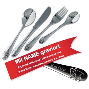Peut inclure: Un ensemble de quatre couverts pour bébé en argent avec un motif d'ours. La coutellerie comprend une cuillère, une fourchette, un couteau et une cuillère avec le texte "Mit NAME graviert" et "Engraved with name / gravé avec le nom grabada con el nombre / incisi con il nome Emilia".