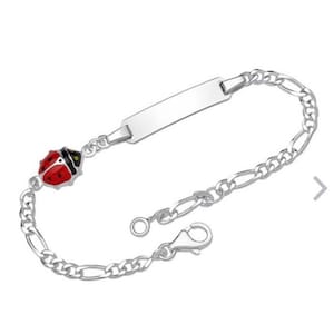 Op de afbeelding: Een zilveren armband met een lieveheersbeestjesbedel en een blanco naamplaatje. Het lieveheersbeestje is rood met zwarte stippen en een zwarte kop. De armband heeft een schakelkettingontwerp en een sluiting.