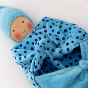 Może przedstawiać: Niebieska i biała w białe kropki lalka niemowlęca z niebieskim kapeluszem. Lalka jest wykonana z miękkiej tkaniny i ma słodką, uśmiechniętą twarz.