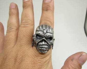 May include: A silver ring with a detailed, three-dimensional design of a face with a helmet. The face has a fierce expression with a wide mouth and sharp teeth.