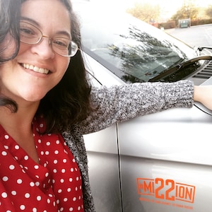 May include: A silver vehicle featuring an orange decal on the side panel with the text #MI22ION and the smaller text UNITED IN THE WAR AGAINST VETERAN SUICIDE. The decal is applied to the smooth, metallic surface of the car door near the front hood.
