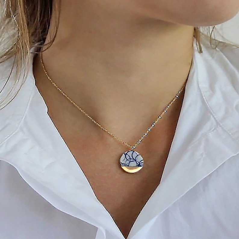 A handmade necklace featuring exquisite blue and white porcelain, adorned with delicate 24k gold accents, elegantly hung on a 14k gold chain. Expert craftmanship. A durable and sustainable jewelry piece. Porcelain jewelry