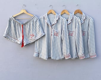 May include: Four gray and white gingham pajamas with red trim. The pajamas have a button-up shirt and shorts. The shirts have the text "E-SS" embroidered on the pocket. The shorts have the number "24" embroidered on the front.
