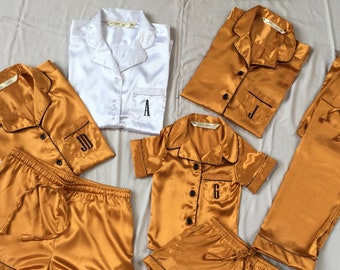 May include: A set of four matching pajamas in a mustard yellow color. The pajamas include a long-sleeved shirt, a short-sleeved shirt, a pair of shorts, and a pair of pants. Each piece has a black embroidered initial on the front.