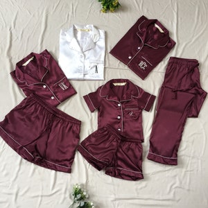K&ouml;nnte beinhalten: Ein passendes Set aus burgunderrotem Satin-Pyjama mit wei&szlig;en Paspeln. Das Set beinhaltet ein lang&auml;rmliges Oberteil, ein kurz&auml;rmeliges Oberteil, eine Hose und zwei Shorts. Jedes Teil hat ein wei&szlig; gesticktes Initial auf der Vorderseite.