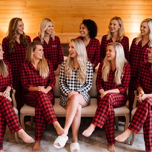 A group of women wearing red and black plaid pajamas are sitting together, smiling and posing for a photograph.