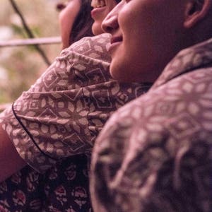 May include: Three people are seen from the shoulders up, smiling. They are wearing patterned shirts in shades of brown and dark blue. The shirts have a repeating geometric and floral design. The image is taken in natural light, with a soft focus.