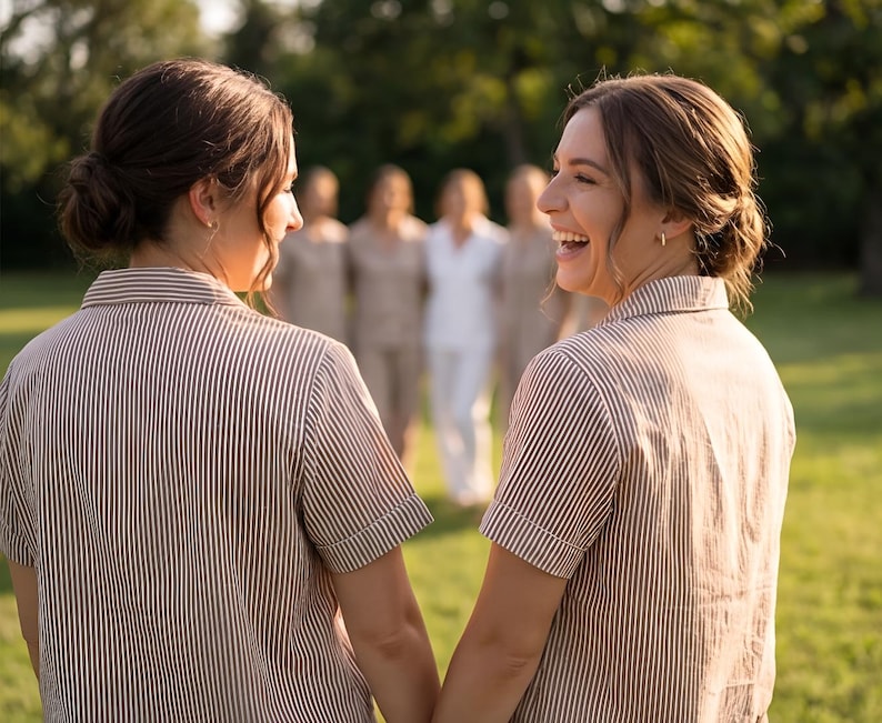 May include: Two people wearing brown and white striped short-sleeved shirts, holding hands, and smiling. In the background, several people are wearing similar outfits. The scene takes place outdoors on a sunny day.