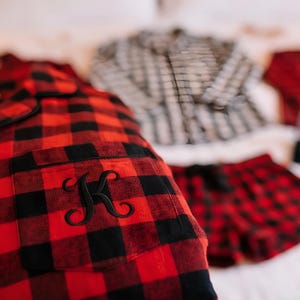 a collection of clothing items, including a red and black plaid shirt with a black "K" embroidered on it, a black and white checkered shirt, and red plaid shorts.