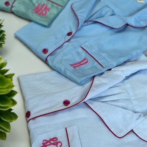 May include: Three light blue pyjama tops with pink piping and pink embroidered monograms. The monograms are "B", "S", and "KHK".