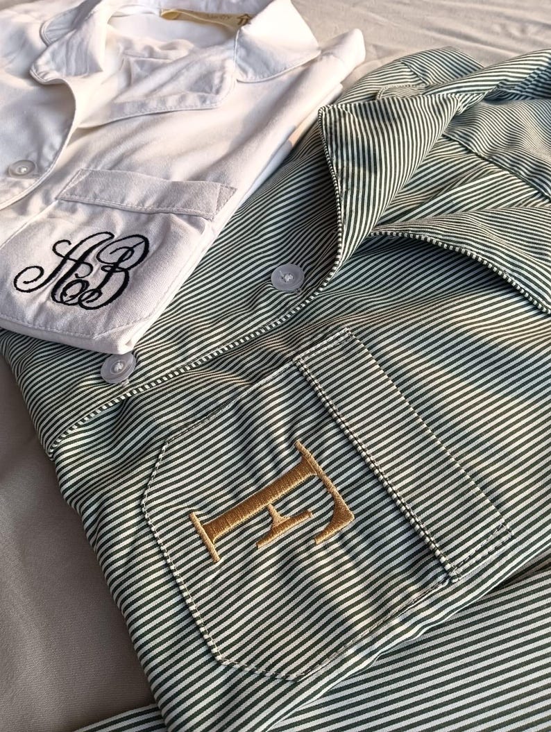 May include: Two pajama tops. One is white with black embroidered initials on the pocket. The other is green and white striped with a gold embroidered initial on the pocket. Both have button closures and collars.