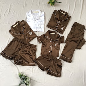 K&ouml;nnte beinhalten: Ein Set aus braunen Satin-Pyjamas mit wei&szlig;en Paspeln und gestickten Initialen. Das Set beinhaltet ein Langarmshirt, ein Kurzarmhemd, eine kurze Hose und eine lange Hose.