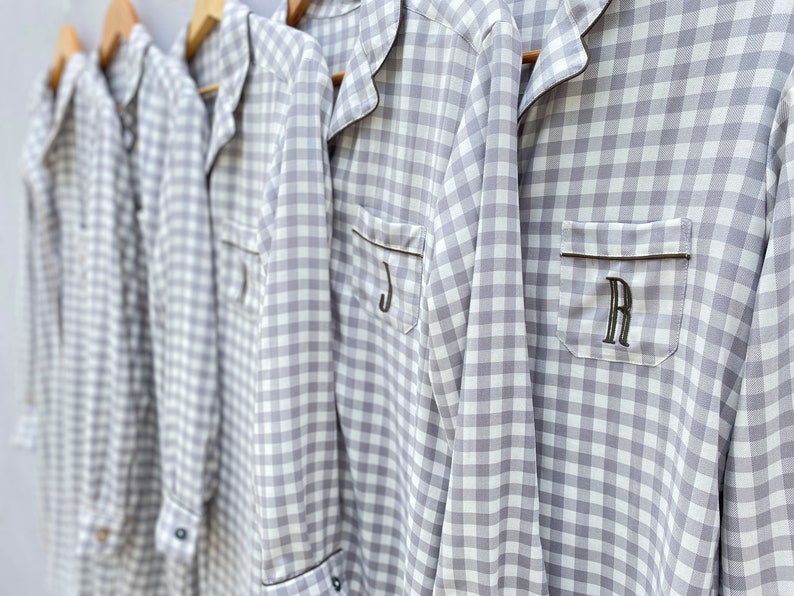 May include: Four gray and white gingham pajamas with black trim and personalized initials. The initials are J, R, and two others.