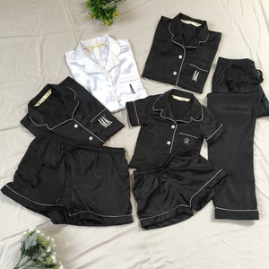 K&ouml;nnte beinhalten: Ein Set aus schwarzen und wei&szlig;en Satin-Pyjamas mit gestickten Initialen. Das Set beinhaltet ein kurz&auml;rmliges Oberteil, Shorts und eine Hose.