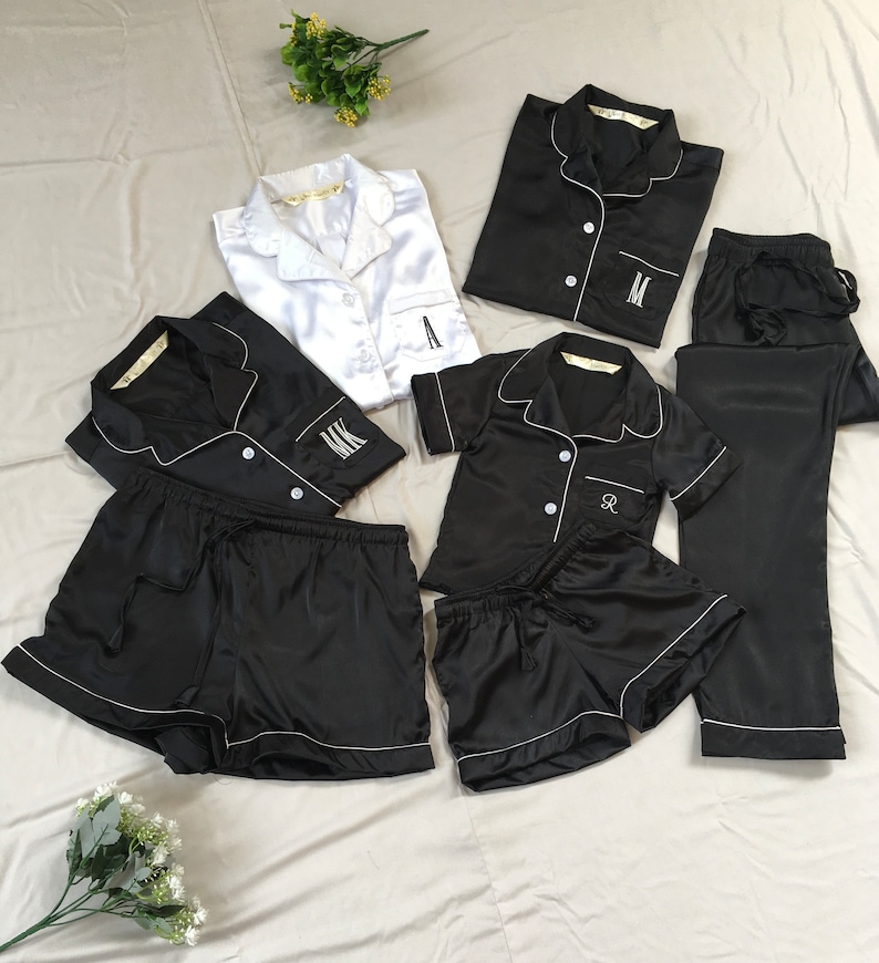 K&ouml;nnte beinhalten: Ein Set aus schwarzen und wei&szlig;en Satin-Pyjamas mit gestickten Initialen. Das Set beinhaltet ein kurz&auml;rmliges Oberteil, Shorts und eine Hose.