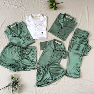 May include: A set of matching pajamas in green and white satin. The pajamas feature a button-up top with a collar and short sleeves. The set includes a pair of shorts and a pair of pants. The tops are personalized with the letters "A", "R", "C", and "GNR".