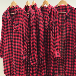 May include: Four red and black plaid shirts hanging on hangers. The shirts are long-sleeved and have a button-down front.