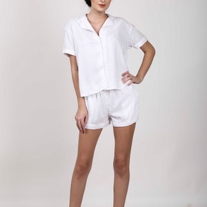 Puede incluir: Un conjunto de camisa blanca de manga corta con botones y pantalones cortos a juego. La camisa tiene cuello y un corte holgado. Los pantalones cortos tienen cintura con cord&oacute;n y dobladillo con vuelta.