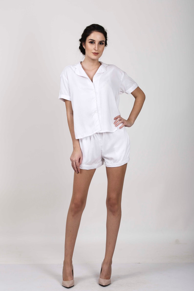 Puede incluir: Un conjunto de camisa blanca de manga corta con botones y pantalones cortos a juego. La camisa tiene cuello y un corte holgado. Los pantalones cortos tienen cintura con cord&oacute;n y dobladillo con vuelta.