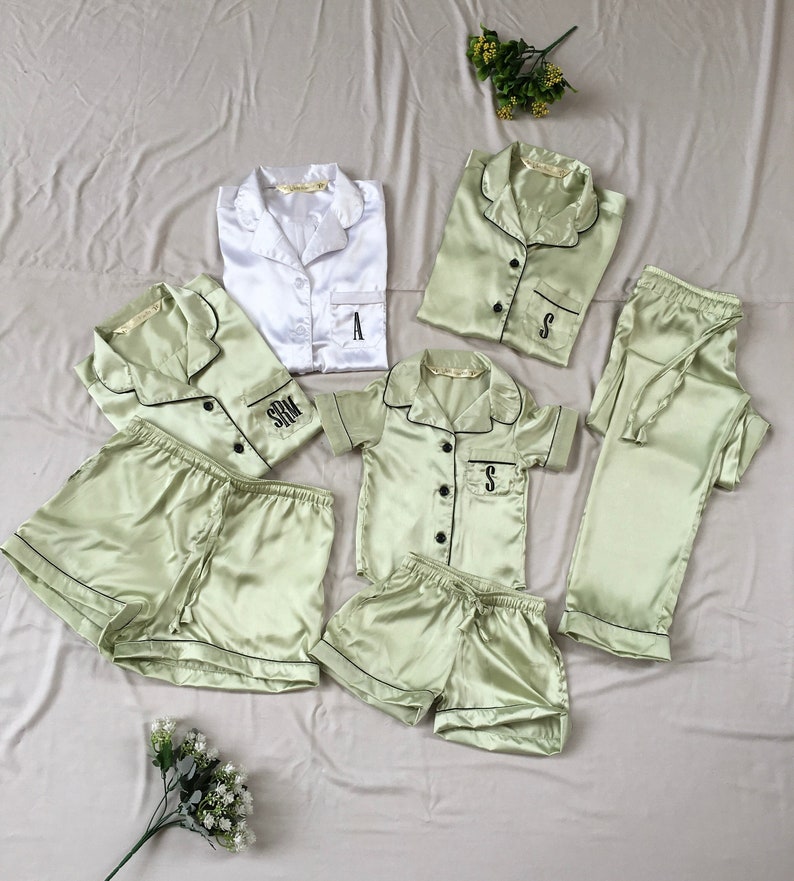 May include: Set of five matching pajamas in a light green color with black trim. The pajamas include a long-sleeved shirt, a short-sleeved shirt, a pair of pants, and two pairs of shorts. Each piece has a different monogram embroidered on the pocket.
