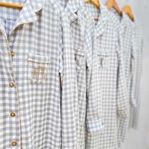 May include: Five gray and white gingham shirts with embroidered initials on the pocket. The shirts are hanging on wooden hangers.