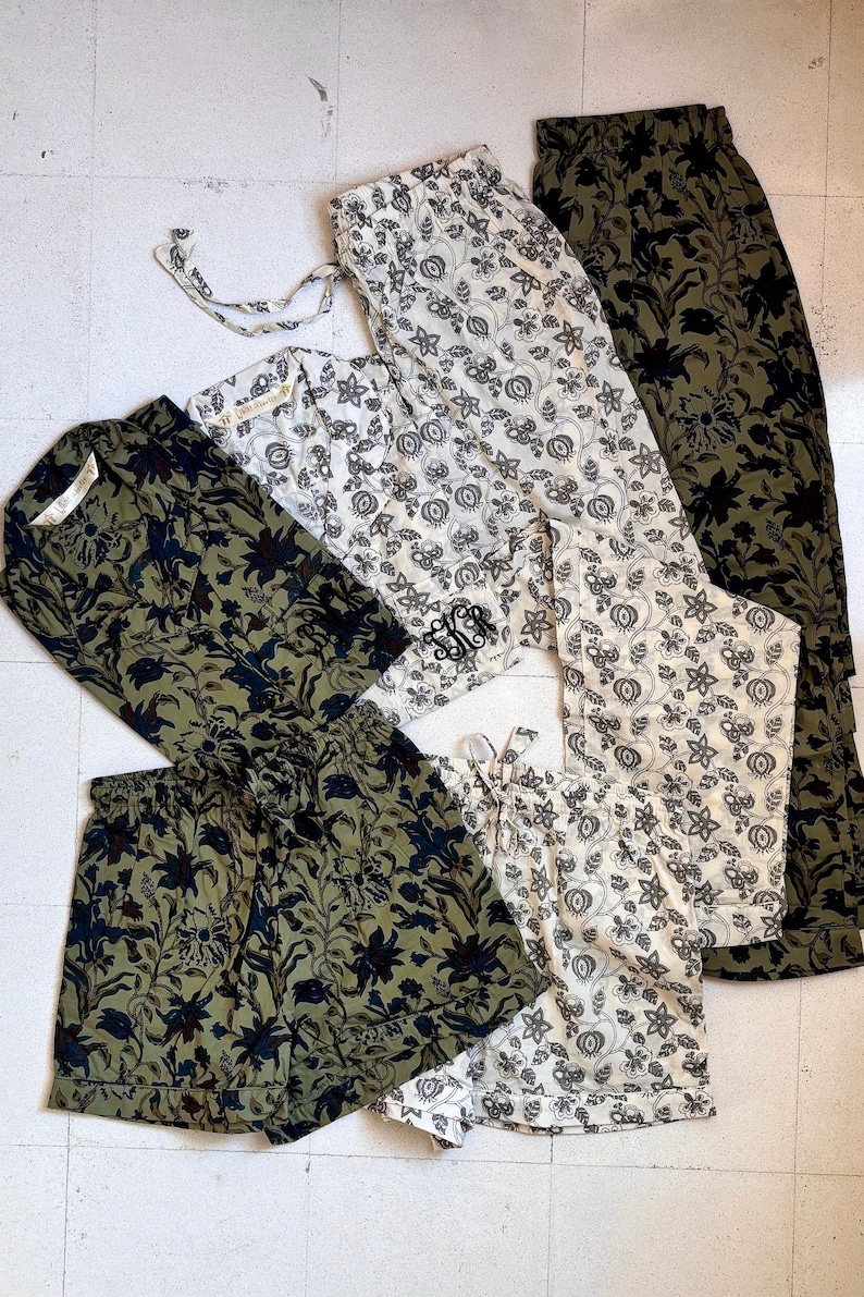 May include: An assortment of floral-patterned sleepwear in various styles and colors. The collection includes shorts, pants, and long-sleeved shirts in olive green, black, and cream. Some pieces feature a monogram.