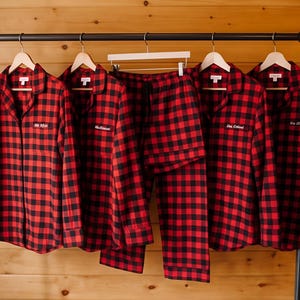 A row of red and black plaid pajamas hanging on a rack, with each pair having a name tag attached to the front.
