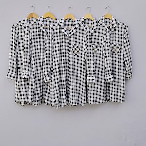May include: Five black and white checkered shirts hanging on hangers. The shirts have a button-down collar and long sleeves.