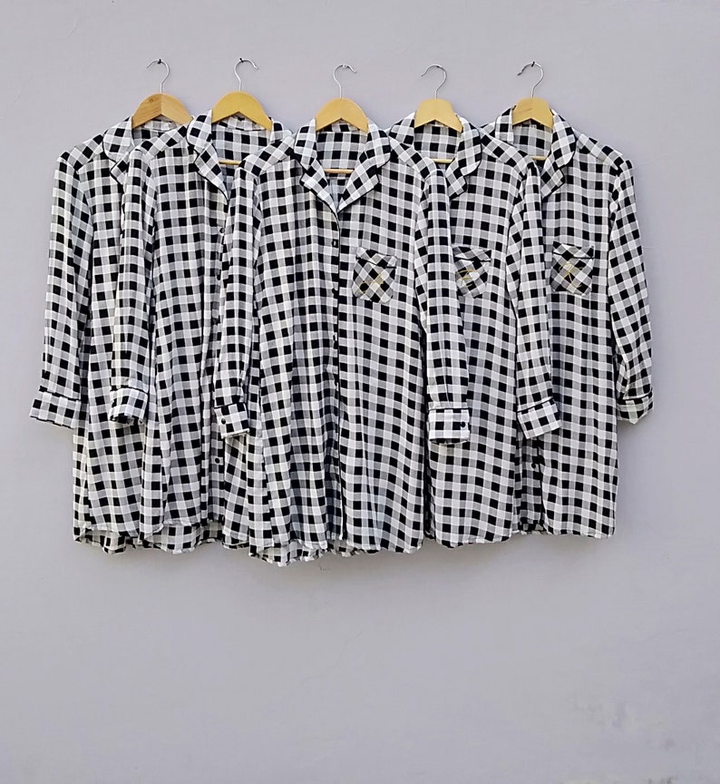 May include: Five black and white checkered shirts hanging on hangers. The shirts have a button-down collar and long sleeves.