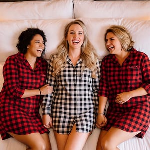 Three women in red and black plaid pajamas are lying on a bed, smiling and laughing together.