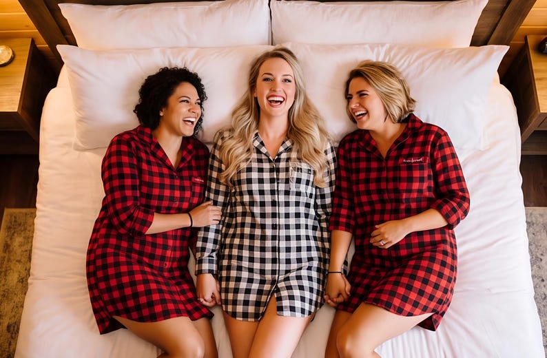 Three women in red and black plaid pajamas are lying on a bed, smiling and laughing together.