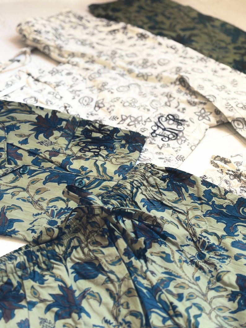May include: Several pairs of patterned pajama pants in various colors. One pair features a blue and beige floral design, another has a white and black floral pattern, and a third is olive green. The pants are laid out on a white surface.