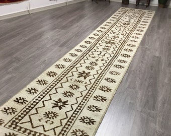 Könnte beinhalten: Ein weißer Läuferteppich mit braunem geometrischem Muster. Der Teppich hat einen Fransenrand und liegt auf einem Holzboden.