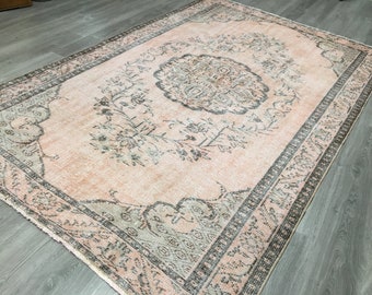 Puede incluir: Una alfombra de estilo vintage con fondo rosa claro y un patrón floral en tonos grises. La alfombra tiene un borde con un diseño geométrico repetitivo.