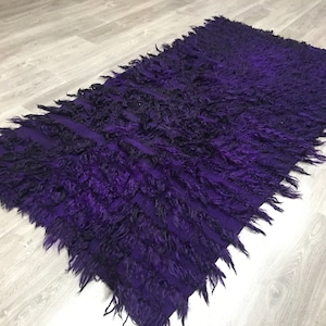 May include: Purple shaggy rug with a gradient of color from dark to light. The rug has a long fringe on all sides.
