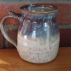 May include: A ceramic mug with a brown, blue, and white glaze. The mug has a rounded body and a handle.