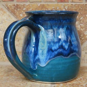 May include: A blue and green ceramic mug with a unique glaze pattern. The mug has a large handle and a rounded body.